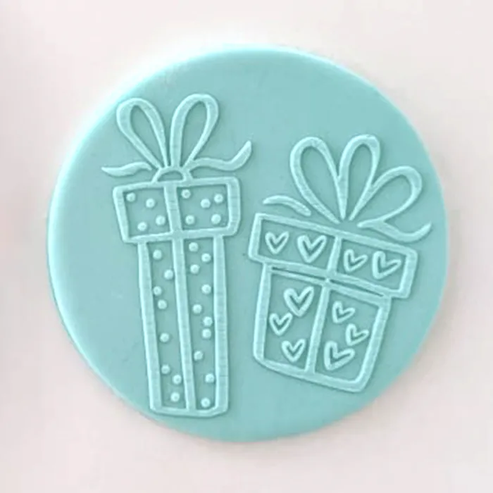 A round light blue fondant circle featuring embossed gift box designs with bows and hearts, shown on a plain light pink background.