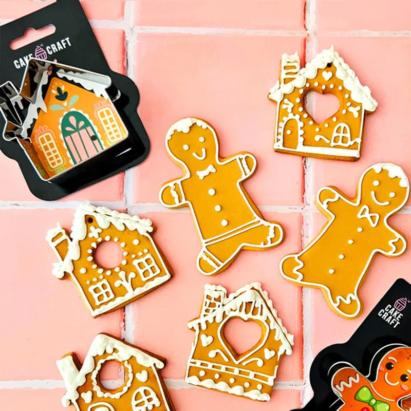 Gingerbread house and gingerbread man cookies on a pink tiled background