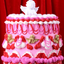 Decorative cake with pink and red icing, white and gold figurines against a red curtain background