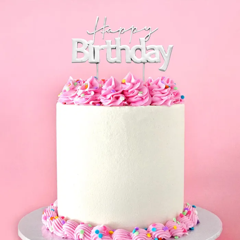 Silver birthday cake with pink frosting and a 'Happy Birthday' topper on a pink background