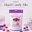 A stand-up pouch of LorAnn Hard Candy Mix centered on a soft lavender background with decorative candy pieces and lavender sprigs around it. Large text at the top reads 'LorAnn Hard Candy Mix' with a tagline below.