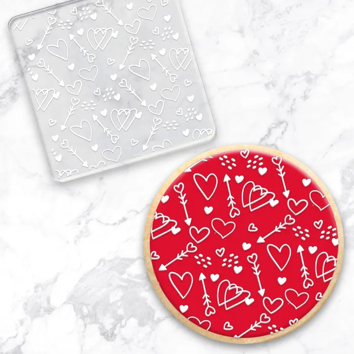 Clear acrylic debosser with a pattern of hearts all over it. Alongside a cookie showcasing the design