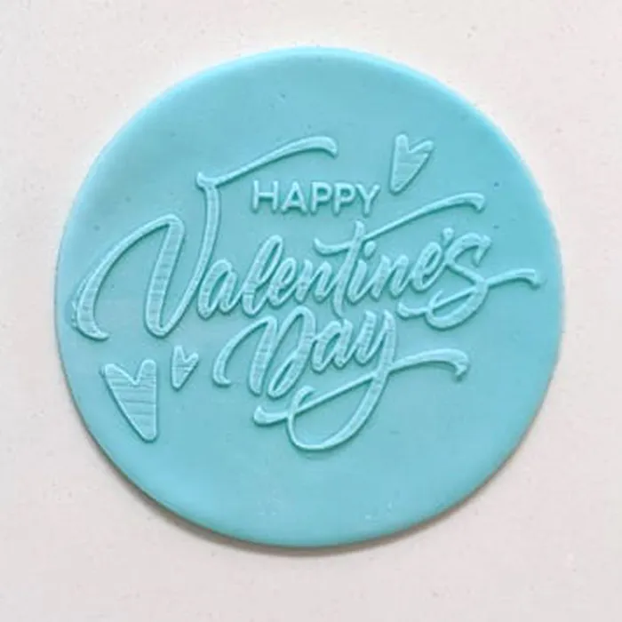 A round light blue fondant plaque with embossed cursive text reading 'HAPPY Valentine's Day' and small heart details, shown on a plain light background.