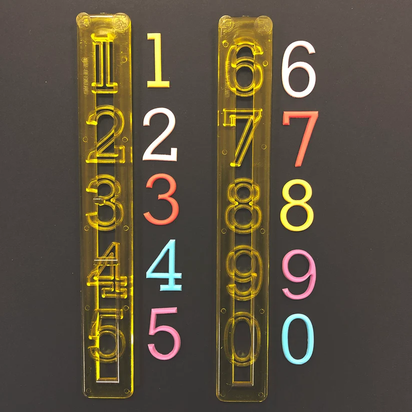 Two transparent yellow plastic number strips shown vertically on a dark background, alongside individual colorful numerals from 0 to 9 in white, yellow, red, blue, and pink.