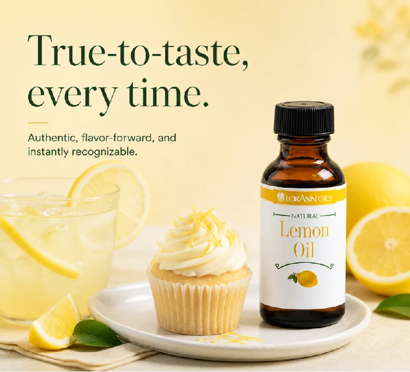 A bottle of Lorann's Natural Lemon Oil stands on a white plate next to a lemon-topped cupcake, with a glass of lemonade and whole lemons in a softly lit kitchen-like setting. Large text reads, 'True-to-taste, every time.