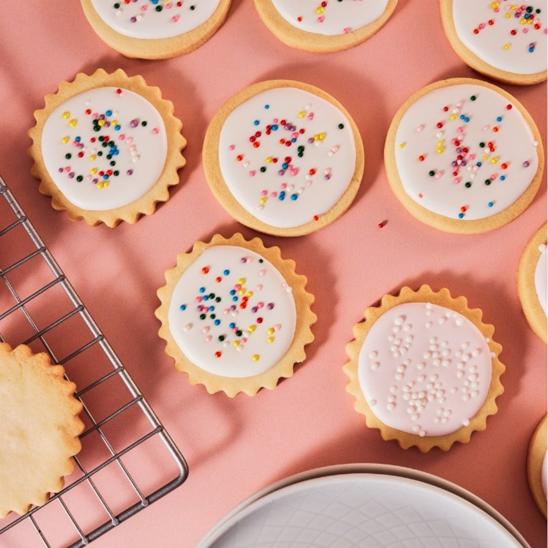 Decorative cookies with white icing and colorful sprinkles on a pink surface.