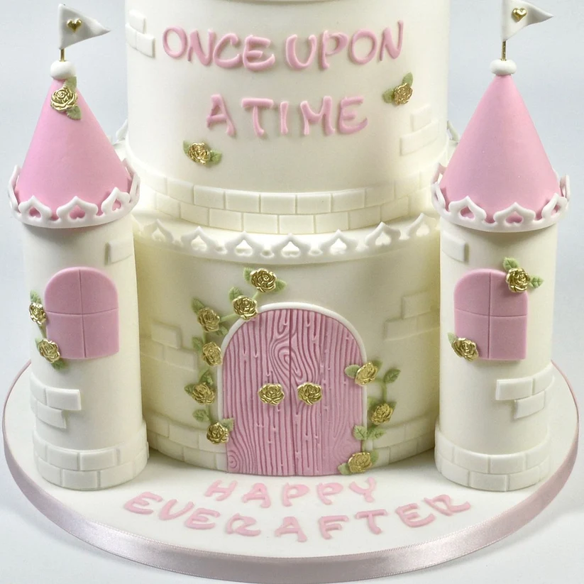 A three-tiered white and pink castle-shaped birthday cake decorated with gold rose details, pink towers, and the words 'ONCE UPON A TIME' and 'HAPPY EVER AFTER' on a white background.