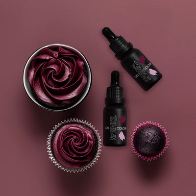 Cupcakes with burgundy frosting and two bottles of 'Sprinks' on a maroon background