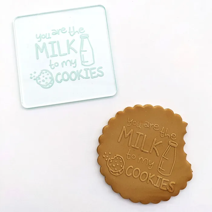 A clear square acrylic or glass stamp with the phrase 'you are the MILK to my COOKIES' and a cookie-and-bottle illustration, shown next to a brown stamped impression of the same design on a white background.