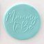 A round, light aqua fondant blue plaque featuring the embossed script text 'Mummy To Be' on a plain white background.