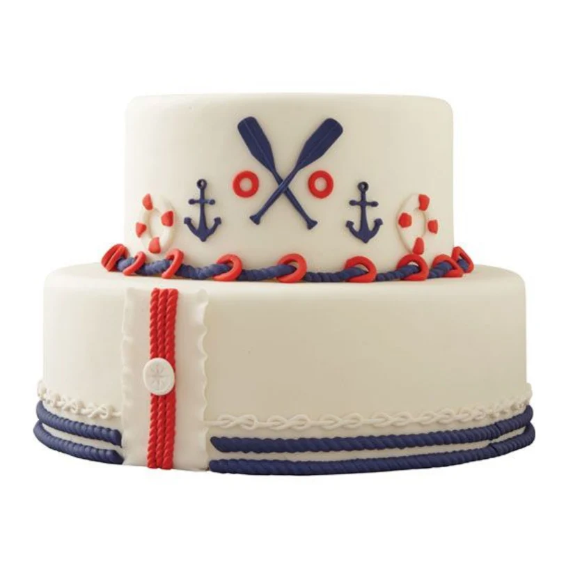 A two-tiered white cake decorated with a nautical theme, featuring navy blue anchors, crossed oars, red and white lifebuoys, and red and navy blue rope details.