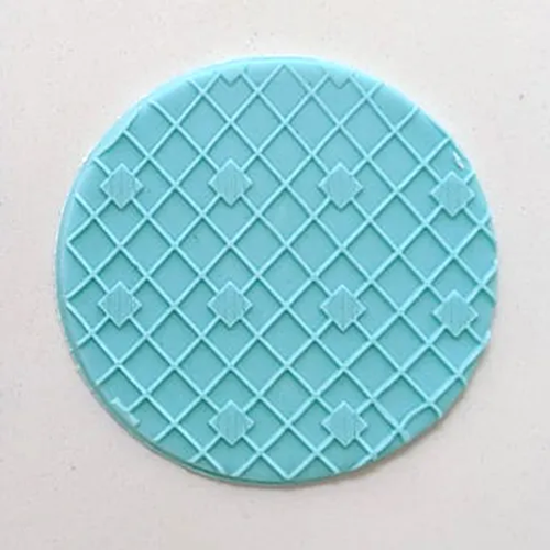 A round light blue decorative fondant piece with a raised diamond lattice pattern and small diamond motifs, shown on a plain off-white background.