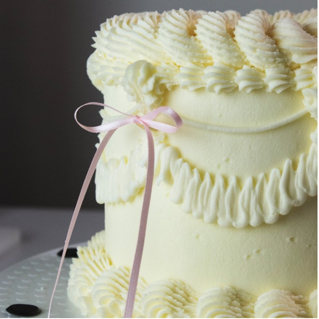 Yellow cake with decorative frosting and a pink ribbon on a dark background
