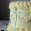 Yellow cake with ruffled texture and a blue ribbon on a dark background
