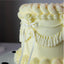 Close-up of a light yellow cake with decorative frosting and a white ribbon against a dark background.