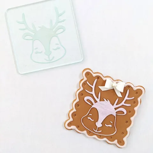 an acrylic debosser with a reindeer head design. Alongside a finished cookie with this design