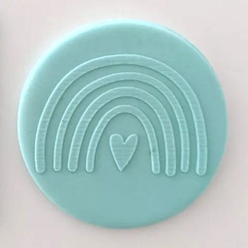 Teal circular fondant plaque with a rainbow and heart design on a light pink background