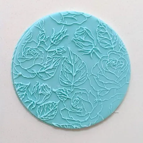 A round turquoise blue fondant icing plaque featuring a raised floral rose pattern, shown on a plain off-white background.