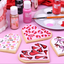 Decorative cookies with heart designs on a pink surface with Colour Mill paint bottles and a palette.