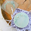 A clear debosser with a floral round frame design, displayedwith a finished cookie, used for imprinting on fondant or gumpaste icing.