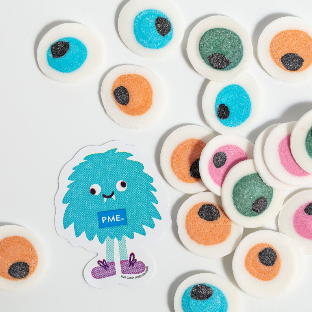 Colorful candy eyes with a small monster sticker labeled 'PME' on a white background