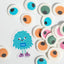 Colorful candy eyes with a small monster sticker labeled 'PME' on a white background