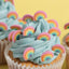 Cupcake with blue frosting and rainbow decorations on a yellow background