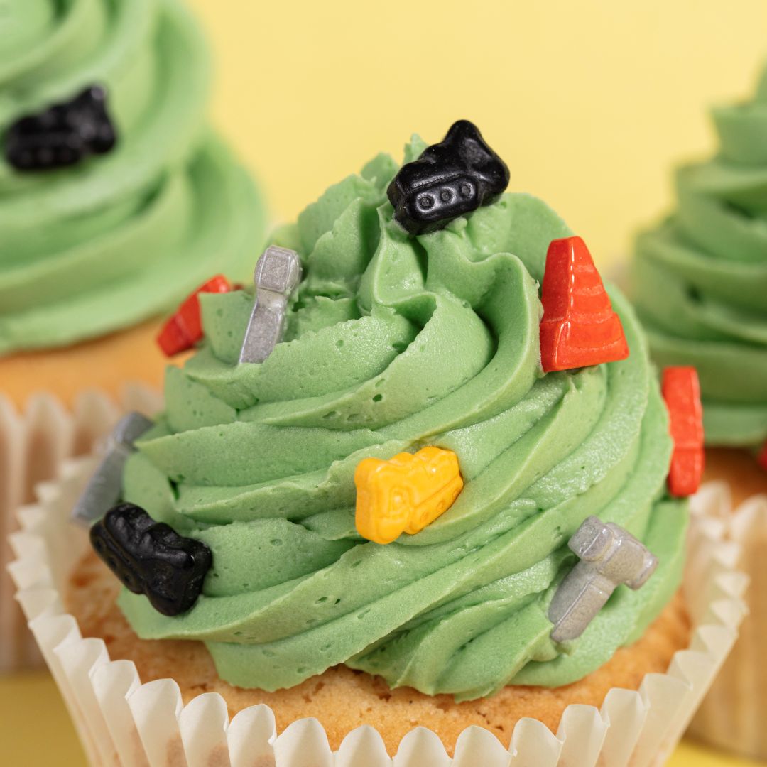 Green frosted cupcakes with construction-themed decorations on a yellow background