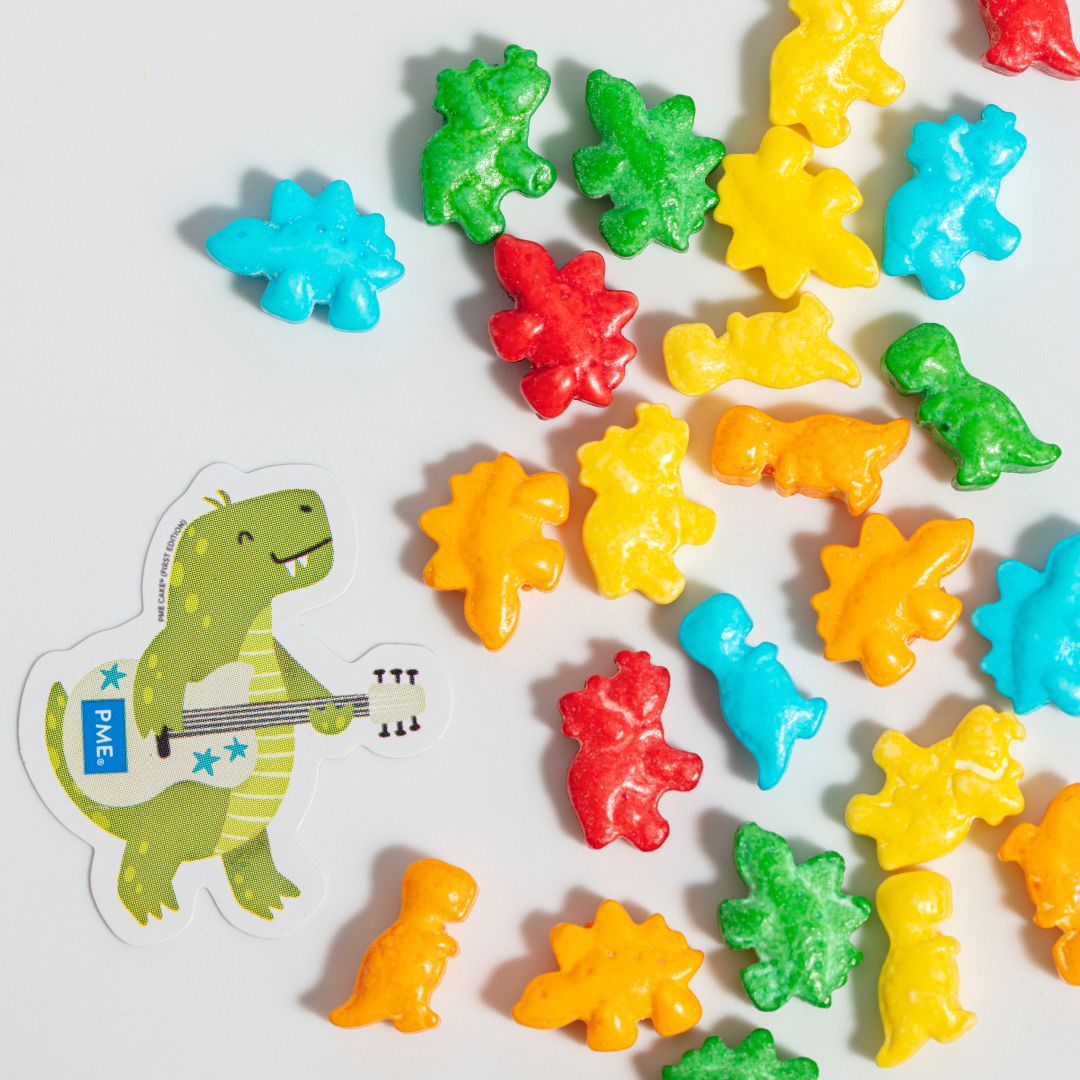 Colorful dinosaur-shaped sprinkles with a sticker of a green dinosaur playing guitar on a white background