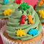 Close-up of a cupcake with green frosting and colorful dinosaur decorations.