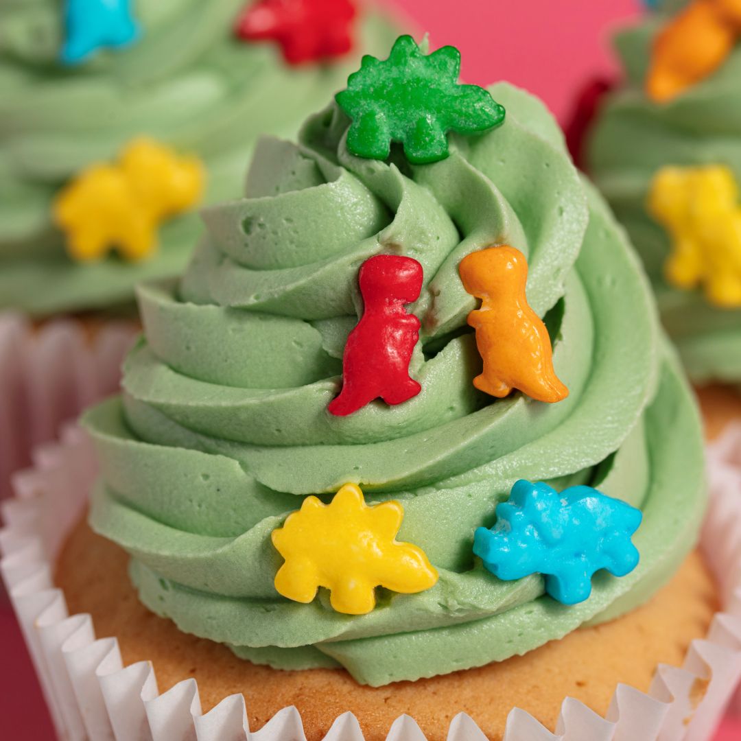 Close-up of a cupcake with green frosting and colorful dinosaur decorations.