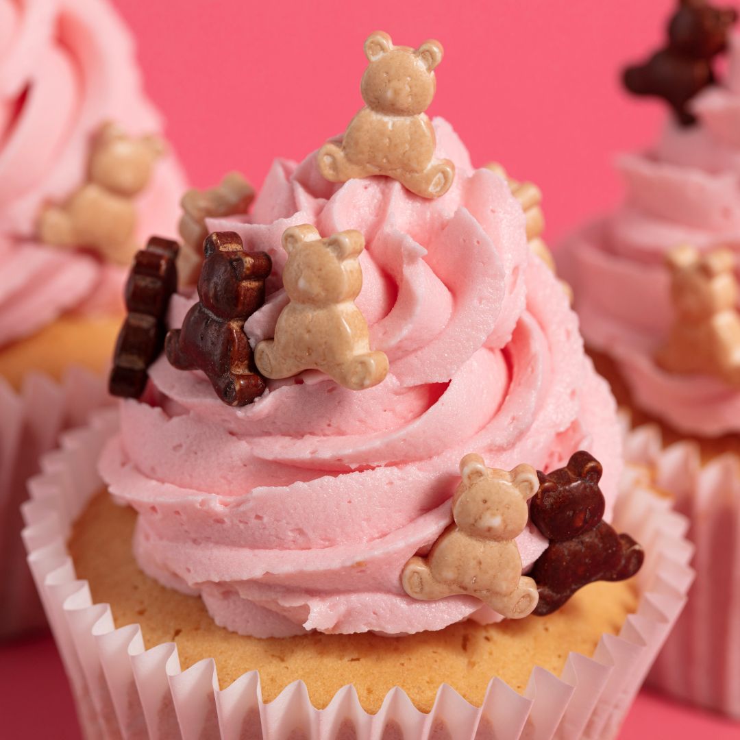 Cupcake with pink frosting and teddy bear decorations on a pink background