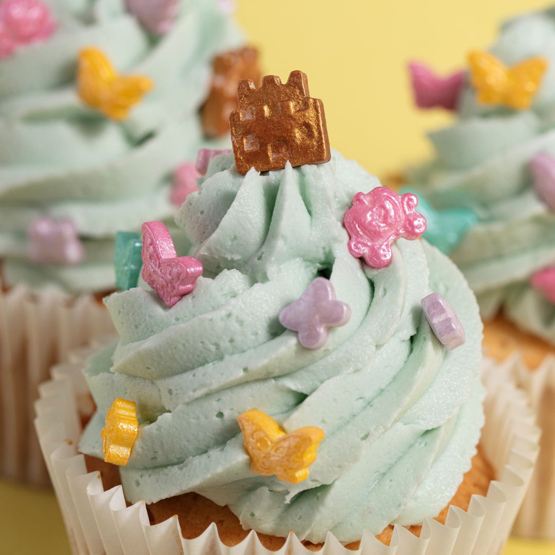 Close-up of a cupcake with green frosting, butterfly decorations, and a castle topper.