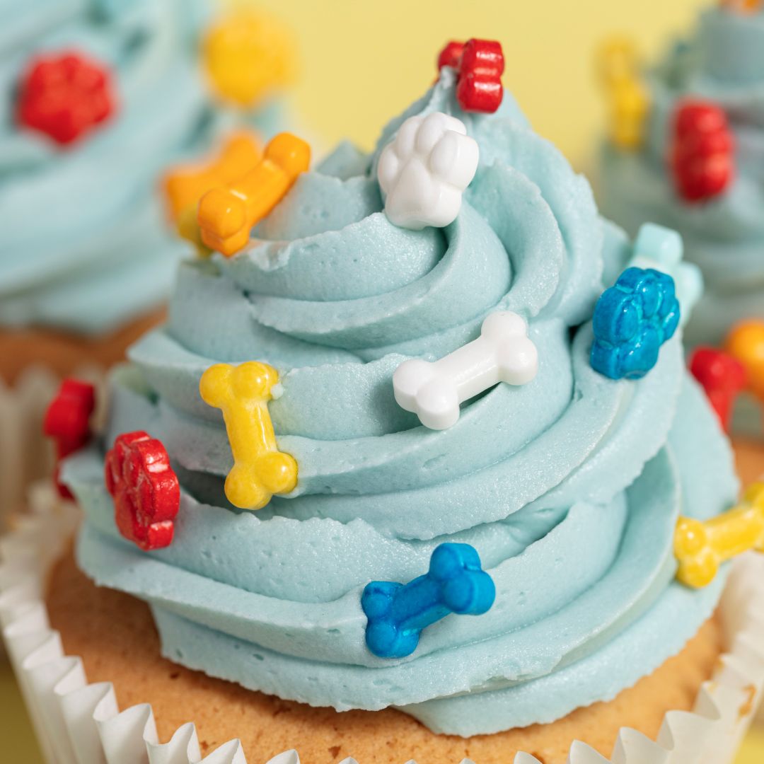 Close-up of a cupcake with blue frosting and colorful dog-themed decorations on a yellow background.