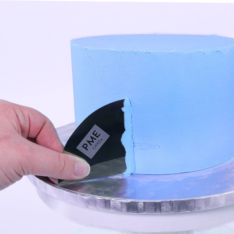 A blue iced cake with a metal scraper creating a pattern