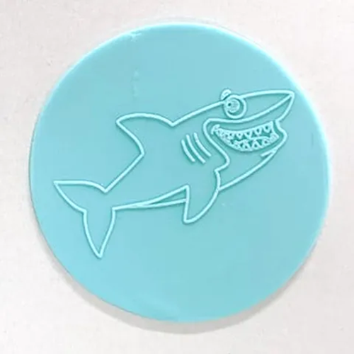 A round blue fondant plaque with a shark outline