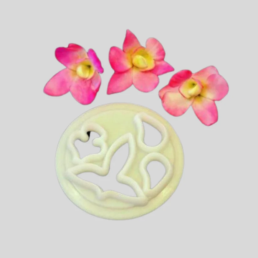 A round pale yellow plastic cutter shown on a light gray background, with three pink-and-yellow orchid flower-shaped cutouts placed above it as examples of the design.