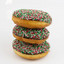 Three stacked donuts with golden-brown fried dough, chocolate glaze, and red, green, and white sprinkles on a white background.