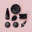 Black Sprinks food colouring including a bottle, bowl, and applicators on a pink background