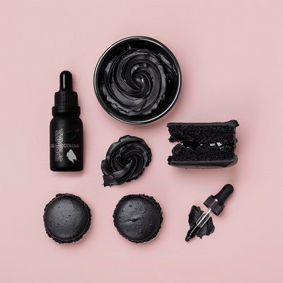 Black Sprinks food colouring including a bottle, bowl, and applicators on a pink background