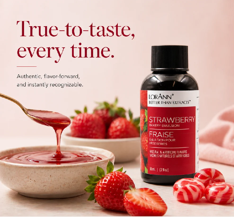 Lorann Better Than Extract Strawberry Emulsion bottle displayed next to a bowl of strawberry jam with a spoon dripping jam, fresh strawberries, and red-and-white striped  candies on a soft pink background.