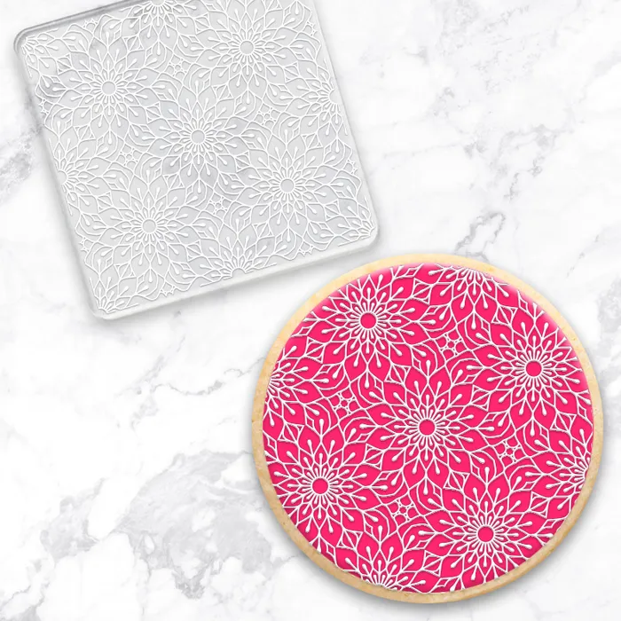 a clear acrylic debosser embossing tool with a pattern of all over flowers. Sitting alongside a finished example made using it of a pink cookie