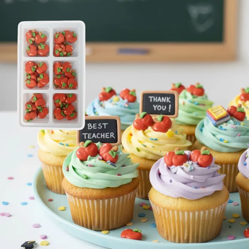 Cupcakes with red apple decorations and small signs on a table with a blackboard in the background.