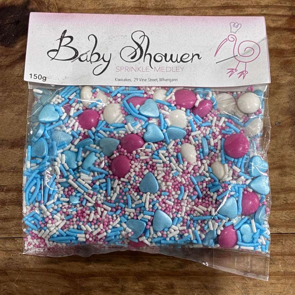 Bag of baby shower sprinkles with pink, blue, and white colors on a wooden surface.