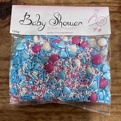 Bag of baby shower sprinkles with pink, blue, and white colors on a wooden surface.