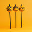 Three Halloween-themed cake pops with jack-o'-lantern faces on a yellow background