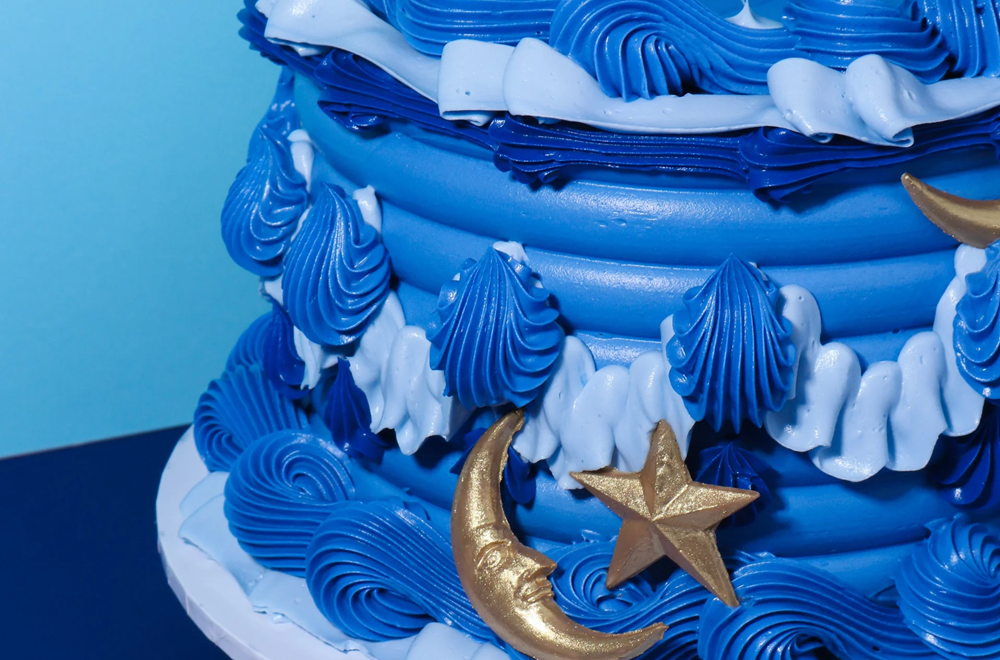 Blue tiered cake with star and moon decorations on a light blue background