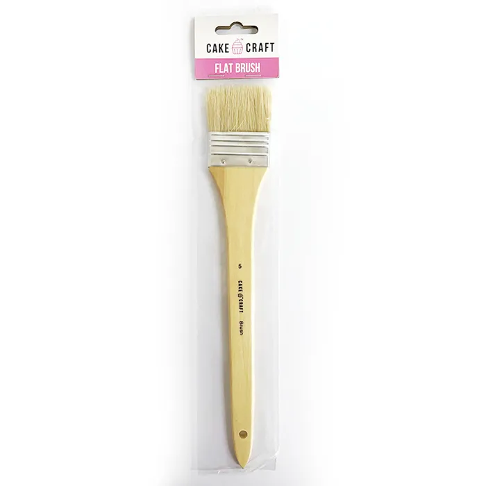A flat craft brush with a light wood handle and natural bristles, packaged in a clear plastic sleeve with a white and pink Cake by Cake Craft header card.