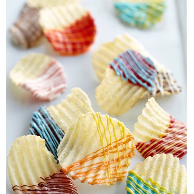 Rimmed potato chips decorated with colorful drizzles of chocolate arranged on a white background.