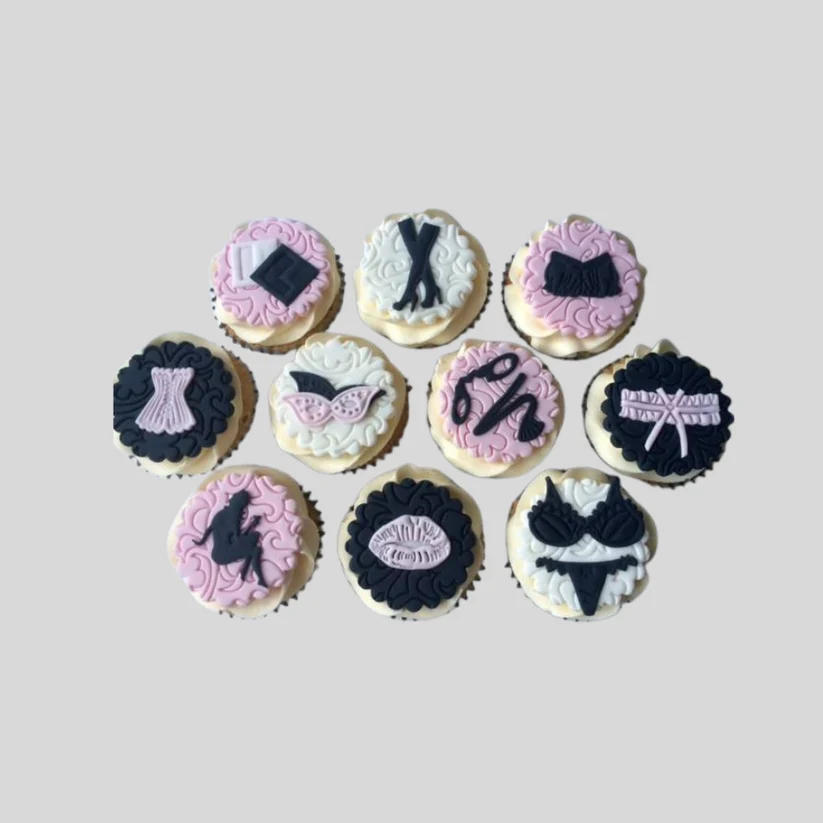 Nine cupcakes decorated with various black and pink fashion-themed sugar sculptures, arranged on a plain light gray background. with cheeky underwear designs